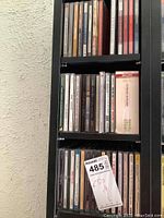 Photo showing several shelves of music CDs in jewel cases on black shelving unit, some visible artist and album names.