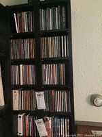 Photo of black shelving unit filled with CDs arranged vertically with visible titles and price tags.