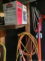 JobMate 1/4 sheet sander boxed with visible label and specifications on box. Shelf in a wooden frame. Includes some hanging hand tools and cords underneath