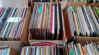 Four boxes filled with vinyl records seen from above, stored vertically in cardboard boxes, showing many album spines