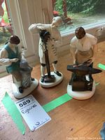 Photo showing three Royal Doulton Williamsburg craftsman figurines arranged on a wooden surface near a window.