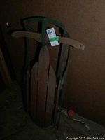 Vintage wooden sleigh with green supports, wooden slats seat, and wooden handles in a corner with dark background.