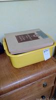 Yellow plastic tub holding the gray Coronet DeLuxe stamp album on a wooden dresser