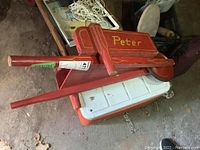 Red wooden child's wheelbarrow with 'Peter' on the side, resting on/or inside the cooler