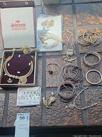 Overall assortment of costume jewelry arranged on table, showing boxed Shreeji Collections set, multiple bracelets, rings, chain necklaces and earrings