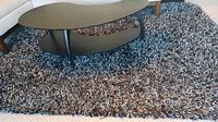 Full view of the black and gray sprinkle shag rug with coffee table on top, showing texture and color blending.