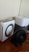 Three appliances grouped on a wooden floor: Vornado fan, Coway air purifier, and Blue air purifier