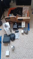 Overview of the lot showing boxes of Duracell AA batteries, cables, Canon camera, and accessories on carpet.