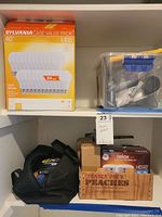 Shelf with Sylvania case value pack LED bulbs, clear container with mounting straps, black bag with tools, and Trader Joe's box containing GE LED bulbs.