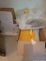 Box containing clear bubble wrap sheets and rolls, yellow padded envelopes, and cardboard book covers stacked neatly.