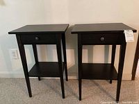 Pair of matching black Ikea Hemnes side tables positioned side-by-side against wall, showing front and top views.