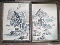 Two framed monochromatic Chinese landscape paintings showing mountains, water, trees, and boats.