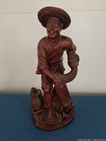 Full view of the antique hand carved Chinese fisherman figurine showing the figure holding a fishing net and standing on a base with fish.
