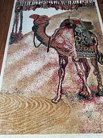 Full view of rectangular vintage area rug featuring camel design with saddle and textured sand-like background.