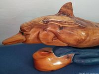 Close-up side view of the carved wooden porpoise's head and front fin, showing wood grain, polish, and some wear.