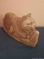 Side angle view showing the detailed sculpted cat resting with bow on neck and visible wear