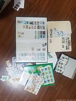 Photo showing multiple stamp albums and folders filled with stamps along with loose stamps spread out.