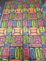Photo of geometric patterned fabric with orange, yellow, red, and black rectangles and squares on wood floor