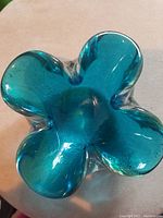 Top view showing unique four-lobed floral shape with teal blue color and smooth glass surface