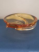 Side view of large amber glass bowl showing curved swirl design and amber tinted edge transitioning to clear base.