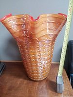 Side view of the vintage hand blown flutter vase showing its textured amber and orange color and approximately 14 inches tall scale.