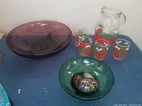 Photo showing vintage amethyst glass bowl, green glass bowl with decorative eggs, and clear glass pitcher with four matching glasses featuring red strawberry and flower decoration.
