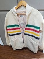 Full front view of vintage Hudsons Bay wool coat on hanger showing multicolored horizontal stripes, zipper, and pockets.