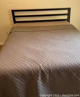 Front view of a double/full metal frame bed with horizontal bars on headboard, covered with a grey quilted bedspread, showing condition and design.