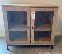 Front view of wooden cabinet showing two glass inset doors and black knobs, with two inner shelves visible through glass.