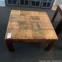 Photo of the square wooden coffee table with natural stained finish and patterned top surface showing wood grain variations and scratches.