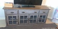 Front view showing the entertainment center with TV on top, three drawers and four glass panel cabinet doors below.