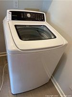 Front and side view of white Frigidaire top-load washer with glass lid closed