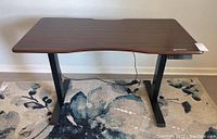 Front view of Harbland adjustable height desk showing woodgrain desktop and black metal legs on floral carpet.