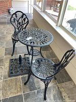View of round metal table with two matching chairs on tiled patio, showing overall style and condition.