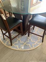 View of round rug under glass dining table with wooden chairs, showing blue base and cream geometric pattern.