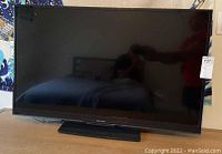 Front view of the Sharp TV with screen turned off, placed on a wooden surface.