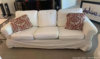 White slipcovered sofa with red patterned pillows on each end, in a living room setting.