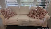 Front view of the white washable slipcovered sofa with four red patterned pillows.
