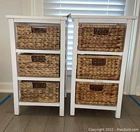 Front view of two white three-tier storage stands with woven baskets, showing natural fiber basket weave and handles.