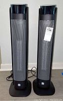 Front view of two WarmWave tower heaters side by side, showing black housing and silver mesh.
