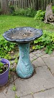 Full view of the green textured leaf pattern pedestal supporting the black leaf-shaped bird bath basin.