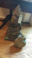 Buddha statue and pottery vase placed on hardwood floor next to black wooden furniture showing overall lot items.