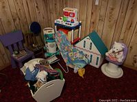 View of the entire toy collection in corner including playhouse, toy kitchen set, white storage bin filled with stuffed toys, and purple chair