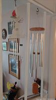 Three wind chimes hanging indoors from white support beam. Presence of wooden wind catcher and multiple metal tubes in varying sizes.