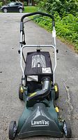 Front view of a green Yardworks LawnVac with black collection bag and metallic handle on pavement.