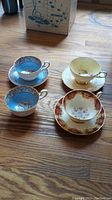 Four fine bone china teacups of varying ornate designs grouped with three saucers, showing overall condition and variety.