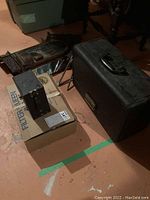 Photo of black storage case, FilterQueen cardboard box with vacuum accessories, and brown antique wooden pendulum clock frame in background.