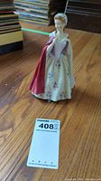 Full view of the Royal Doulton figurine standing on a wooden floor with visible detailed dress and cloak.