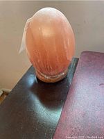 Pink Himalayan salt lamp, oval shaped, sitting on a circular wooden base with visible wear.