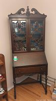 Full view of antique secretary desk including the glass front cabinet, drop-front desk, and carved wood details.